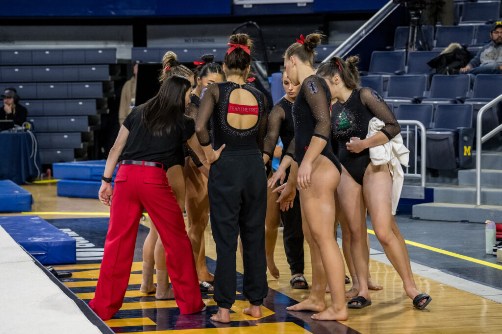 The Stanford women's gymnastics team huddles during a meet against Michigan in their "Angry Tree" leotards.