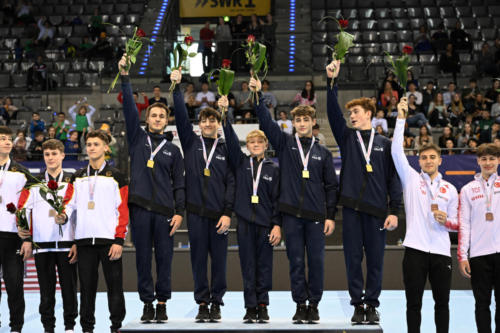 The U.S. team wins gold in the junior men's Team Challenge at the 2023 DTB Pokal. From left to right: Alex Nitache (GymTek), Zach Green (Stanford Boys), Danila Leykin (EVO), Solen Chiodi (Mini-Hops), and Max Odden (North Valley). (© Filippo Tomasi)